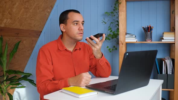 Young Man Recording Voice Message on Smartphone in Home Office