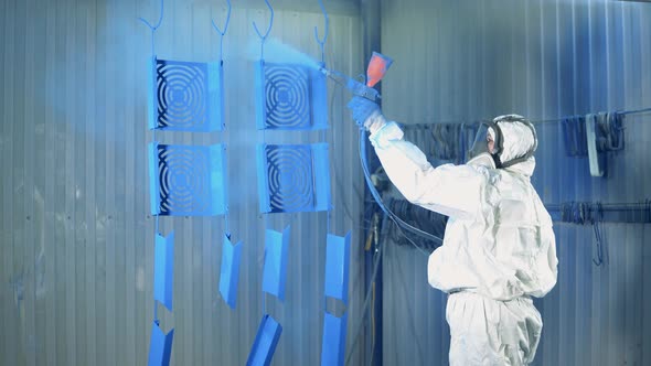 Blue Paint is Getting Sprayed Onto Metal Plates By a Female Worker alt
