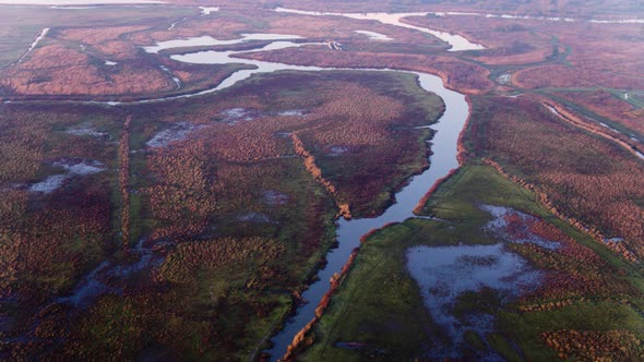 Scenic river delta through misty reddish reed and flooded farmlands; drone alt