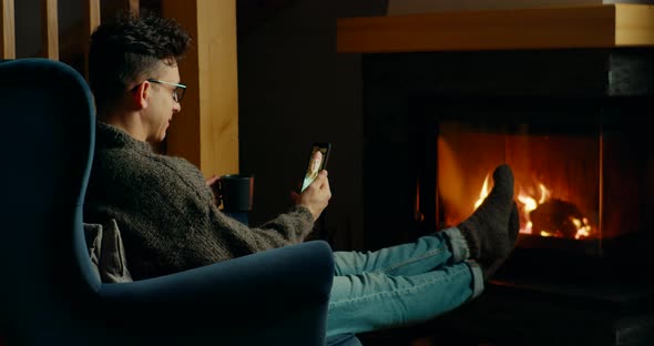 Man Makes Online Video Call By Smartphone and Talks with Woman at Fireplace