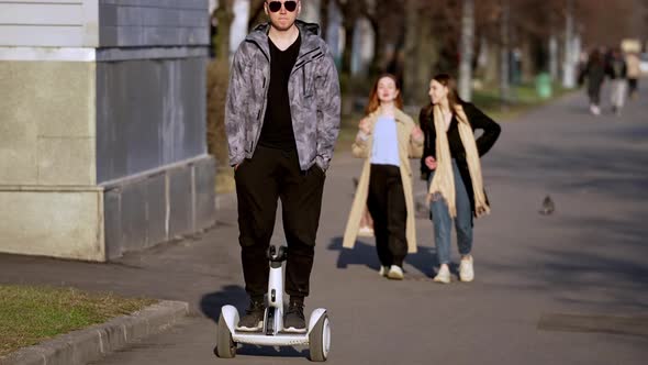 a Young Man in Sunglasses is Having Fun Riding a Hoverboard in Early Spring on a Bright Sunny Day alt