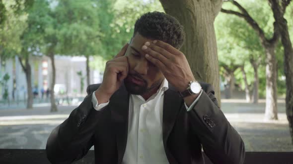 Tired Businessman Talking on Smartphone in Park alt