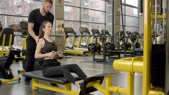 Young Woman with Instructor Working Out in Gym By Using Rowing Machine