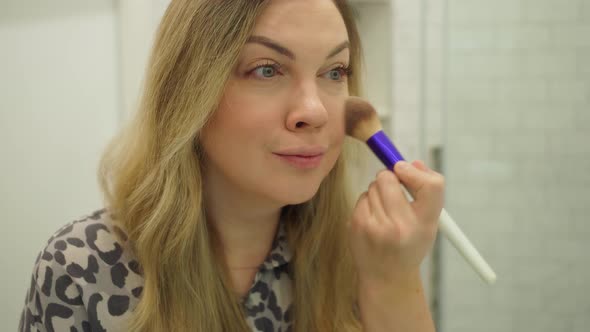Beautiful Young Woman Doing Makeup with a Big Fluffy Brush in the Bath in Front of a Mirror Closeup alt