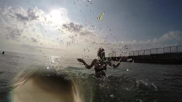 Silhouette of the Girl in the Sea. She Joyfully Squirting Water into the Camera alt
