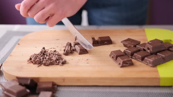 Woman Chopping Black Dark Chocolate on Wooden Cutting Board alt
