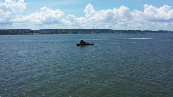 A low angle drone view over Lower New York Bay. The drone truck right & pan left around a tugboat wi alt