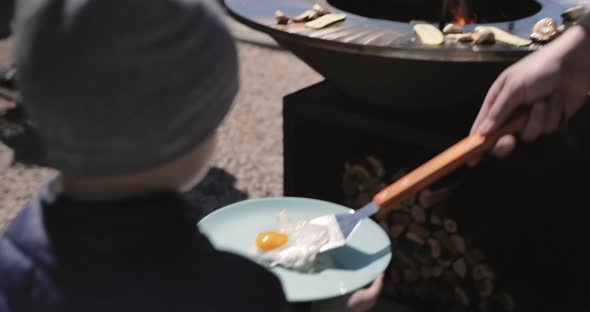Father cooking breakfast for son. Fried eggs, cabbage, mushroom grilled on bbq grill. alt