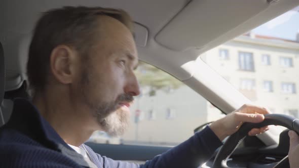 A Middleaged Handsome Caucasian Man Drives a Car Through an Urban Area  Side Closeup