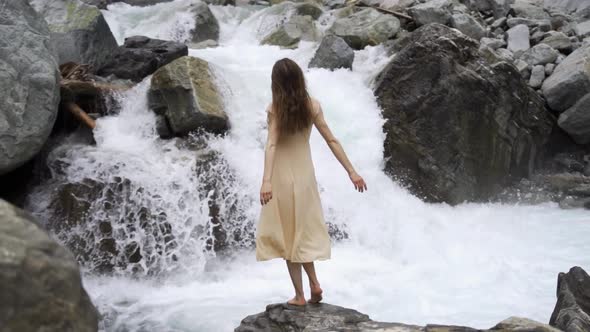 Young Woman in a Light Dress Against the Background of a Waterfall