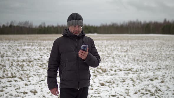 Man in Shabby Winter Jacket Having an Online Video Chat Standing in a Rural Field in Winter
