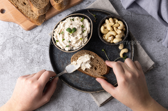 Female hands spreading vegan cashew cheese on a slice of bread.