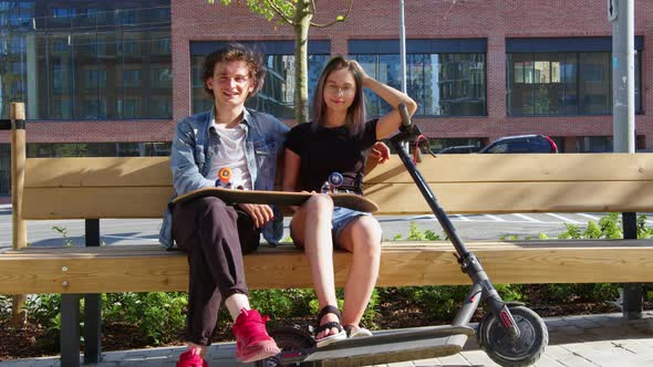 Guy Girl Sit on Bench with Skateboard Escooter alt