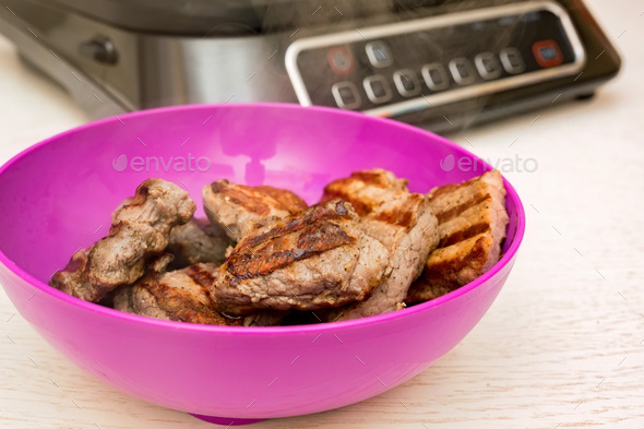 Close-up cooked pork meat on the table near electric grill - Stock Photo - Images