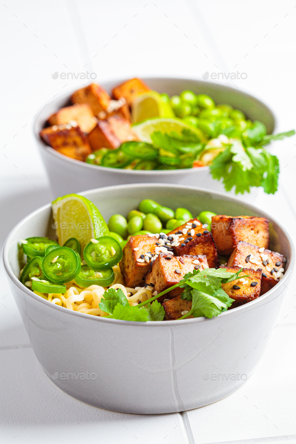 Vegan noodles ramen soup with marinated tofu, edamame beans and hot peppers in gray bowls.