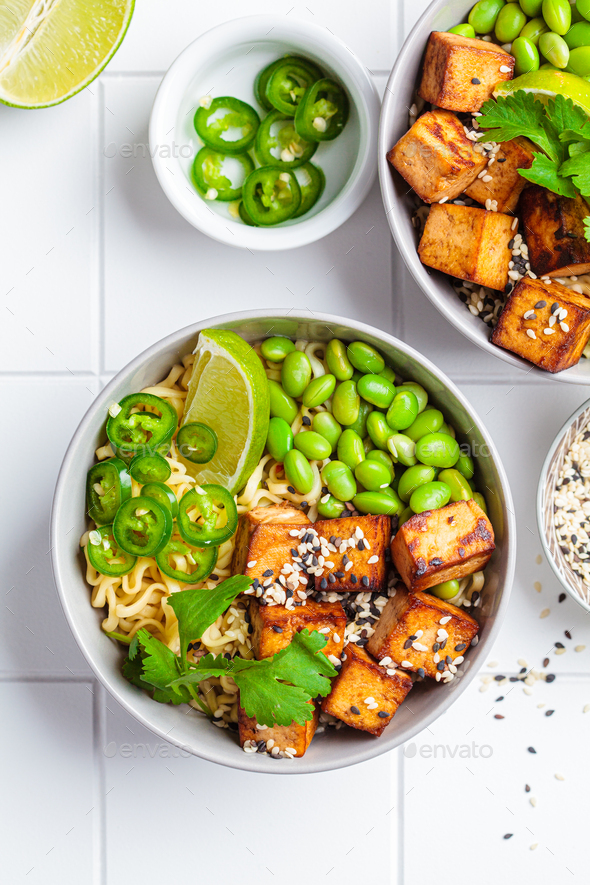 Vegan noodles ramen soup with marinated tofu, edamame beans and hot peppers in gray bowls.