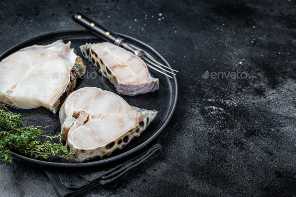 Fresh Raw wolffish o wolf fish Steak on a plate. Black background. Top view. Copy space