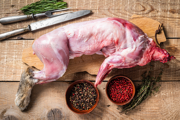 Raw Whole wild hare, fresh game meat on wooden board with herb. Wooden background. Top view