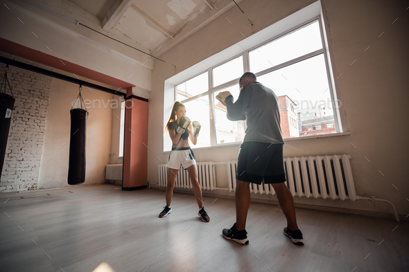 Female martial arts fighter practicing with trainer, punching taekwondo kick pad exercise kicking