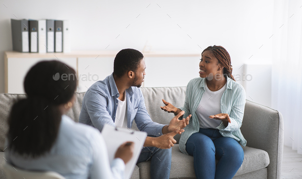 Young black couple having conflict during marital therapy with psychologist at office, panorama