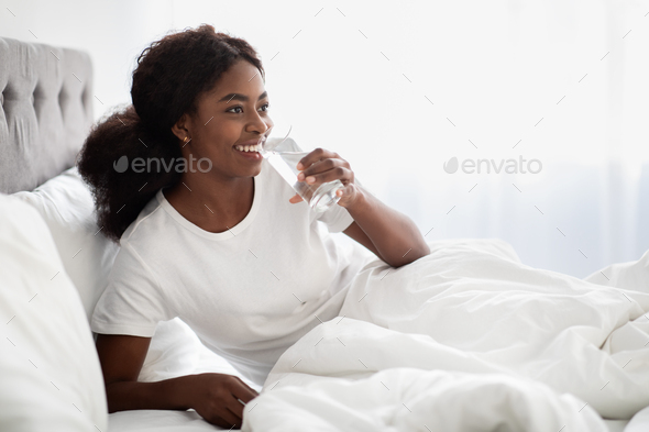 Smiling pretty black lady drinking water in bed