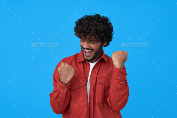 Excited young indian guy winner celebrating win isolated on blue background.