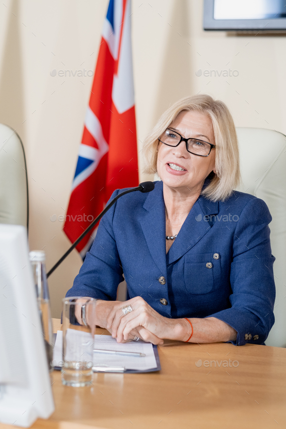 Confident mature blond female delegate speaking at conference