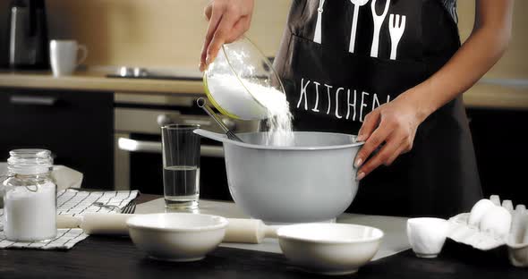 Woman in an Apron Pours Flour and Soda Into a Gray Bowl in a Modern Kitchen