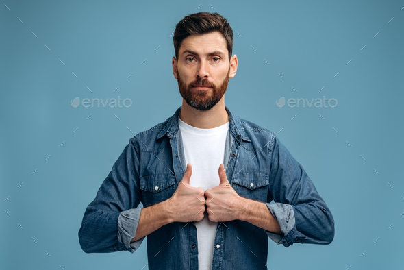 Calm serious man with beard in cool clothes showing thumbs up gesture, expressing satisfaction