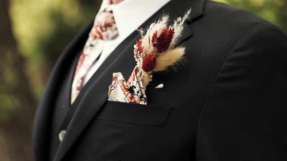 Young Man or Groom Standing Outdoors in a Formal Black Suit with Unique Boutonniere and Patterned Ti alt