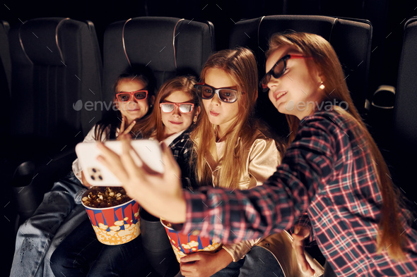 Holding phone in hand. Group of kids sitting in cinema and watching movie together