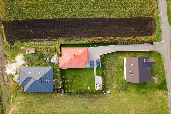 Aerial top view of house shingle roof with attic windows and cars on paved yard with green grass