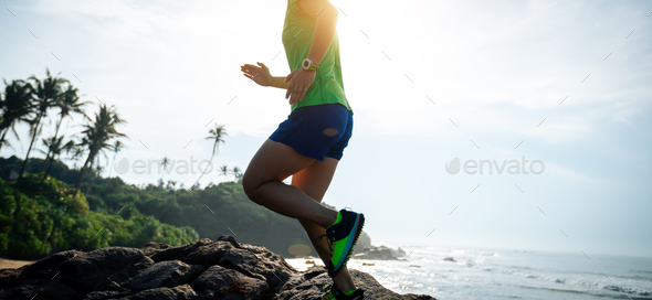 Woman trail runner running to rocky mountain top on sunrise seaside