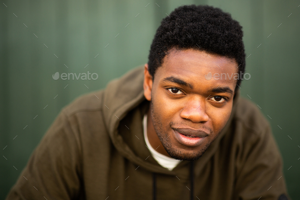 Close up serious young black man staring by green wall