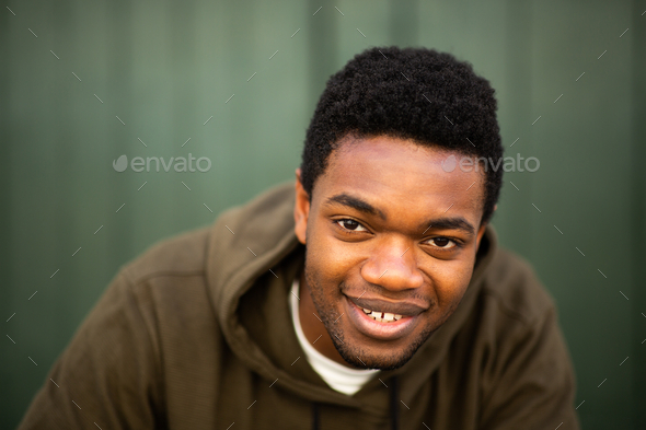Close up smiling young black man staring by green wall