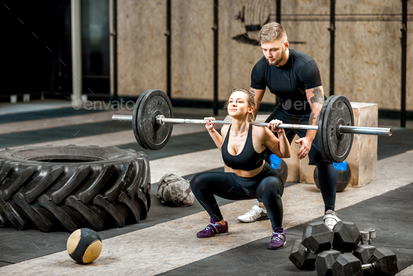 Woman lifting up a burbell with coach in the gym