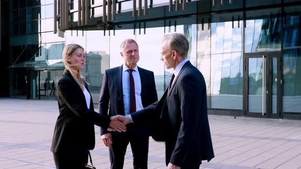 Businessmen and Businesswoman Meet a Coworker and Shake Hands Then Talk. Modern Office Building on