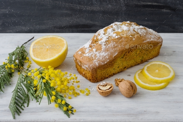Lemon cake with nuts on a wooden white surface, a twig of mimosa flowers