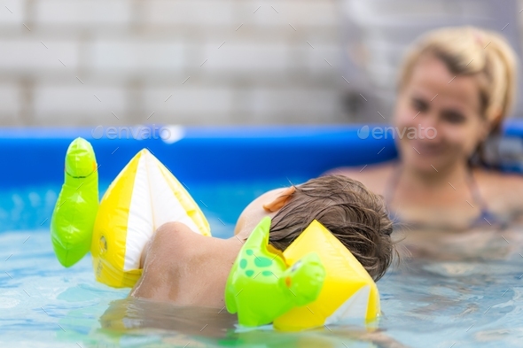 Mom plays with a naked baby in oversleeves in the pool against the  background of a summer sunset Stock Photo by YouraPechkin