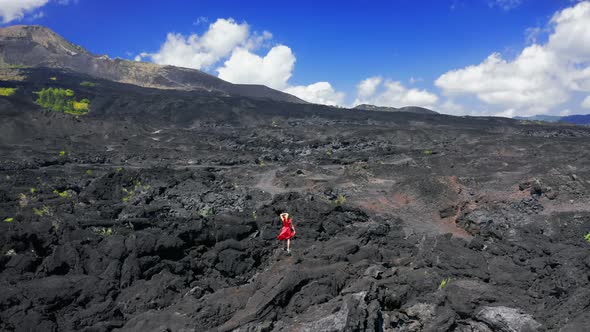 Woman in Red Dress on Solidified Lava Field Near Volcano Batur in Bali, Indonesia. Aerial View  alt