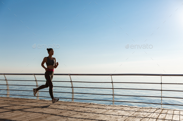 Side view of attractive and healthy fitness woman running along the seaside  promenade. Girl jogging Stock Photo by benzoix