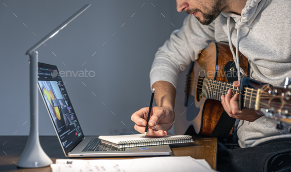 A man with a guitar in front of a laptop at a late hour learns to play.