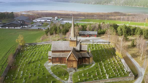 Tilt-Down Of Lom Stave Church With Cemetery In Green Meadows During Snowstorm In Norway. Aerial alt