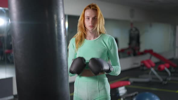 Medium Shot of Fit Strong Woman Hitting Boxing Gloves Posing in Gym Indoors alt