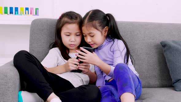 Two happy cute little girls using smartphone for playing or studying together at home