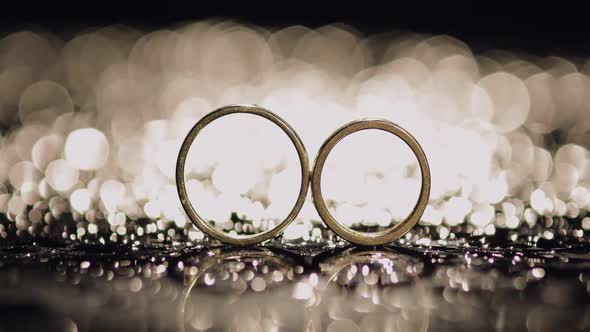Wedding Rings on Dark Water Surface Shining with Light. Close Up Macro alt