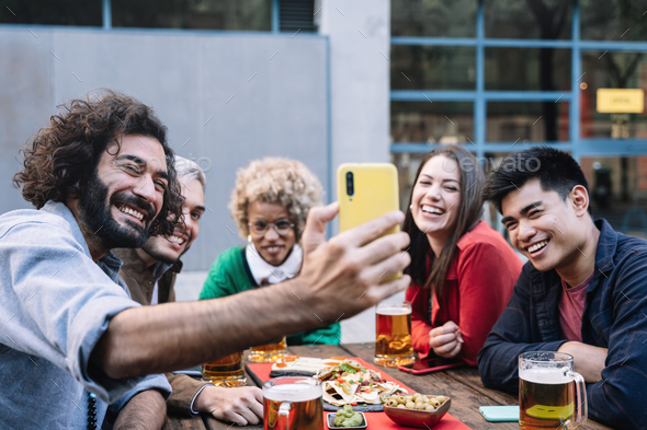Group happy friends taking selfie photo in outdoors restaurant bar to share celebration