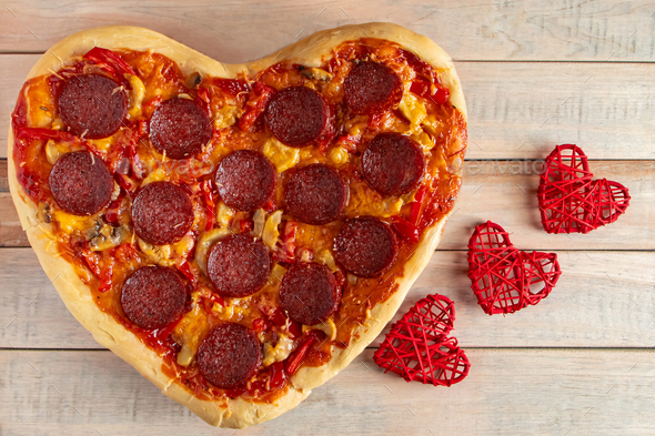 Heart shaped pepperoni pizza on a wooden background.