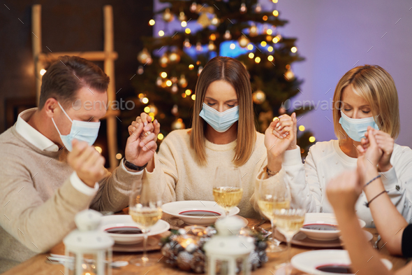 Friends praying before christmas dinner wearing mask.