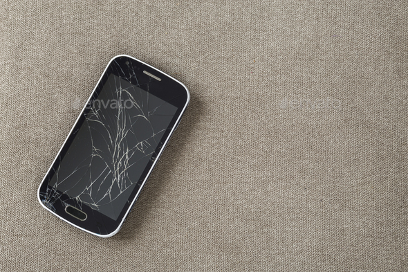 Black old cellphone with cracked screen on light cloth copy space background. Gadget repair and